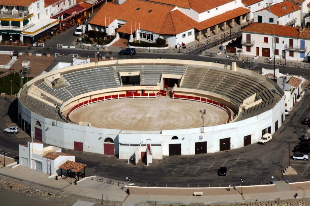 Vue aérienne des Arènes - Ville côtière Arènes (bullring) blanches vues du ciel, gradins, piste sable. Bâtiments toit tuile orange. Textes: PRESIDENCE, TORIL.